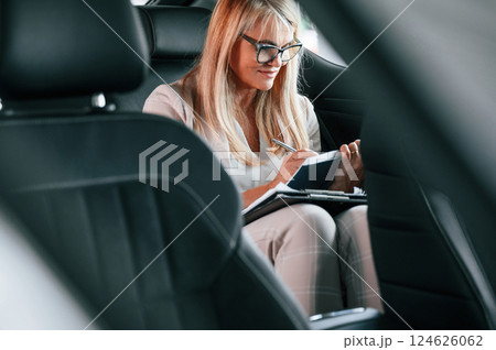 Sitting on the backseat and working. Woman in white formal clothes is in the car dealership 124626062