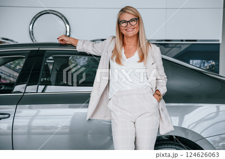 With beautiful new automobile. Woman in white formal clothes is in the car dealership 124626063