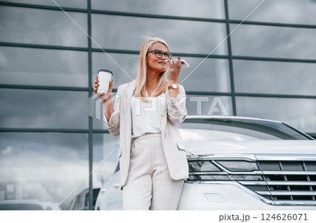 Standing against building with big windows. Woman in white formal clothes is in the car dealership 124626071