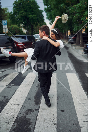 Man holding his woman in hands. Beautiful bride with his fiance is celebrating wedding outdoors 124626237