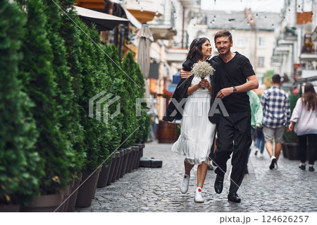 On the street with green plants on the left side. Beautiful bride with his fiance is celebrating wedding outdoors 124626257