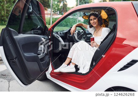 Sitting in white and red colored car. Bride in dress is outdoors before her wedding begins Sitting in white and red colored car. Bride in dress is outdoors before her wedding begins 124626268
