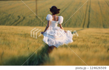 Rear view. Beautiful young bride in white dress is on the agricultural field at sunny day 124626509