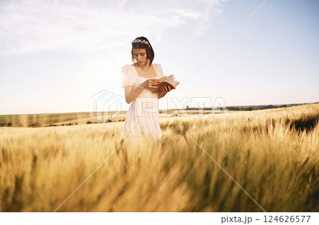 With book in hands. Beautiful young bride in white dress is on the agricultural field at sunny day 124626577