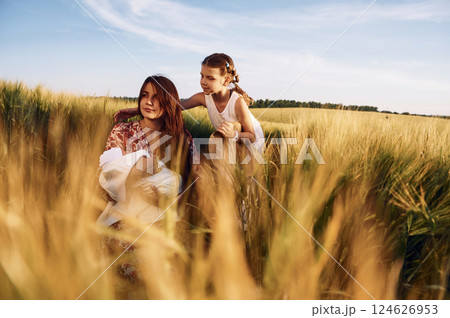 Woman is sitting on the ground. Mother with her newborn baby and girl is on the field at sunny day together Woman is sitting on the ground. Mother with her newborn baby and girl is on the field at sunny day together 124626953