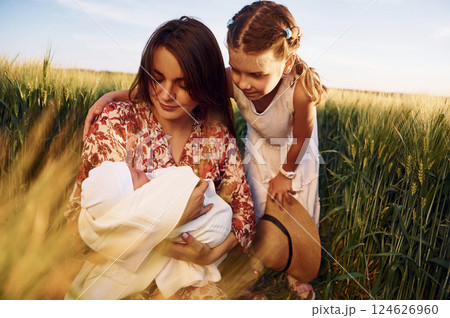 Looking at the newborn baby. Mother with girl is on the field at sunny day together 124626960