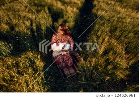 Sitting on the ground. Gorgeous woman is on the agricultural field with her newborn baby 124626961