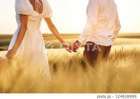 Walking and holding each other by the hands. Couple just married. Together on the majestic agricultural field at sunny day Walking and holding each other by the hands. Couple just married. Together on the majestic agricultural field at sunny day 124626999