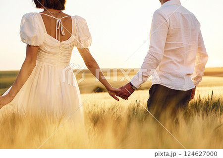 Walking and holding each other by the hands. Couple just married. Together on the majestic agricultural field at sunny day Walking and holding each other by the hands. Couple just married. Together on the majestic agricultural field at sunny day 124627000