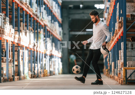 Kicking soccer ball. Storage worker is in the warehouse with bunch of products Kicking soccer ball. Storage worker is in the warehouse with bunch of products 124627128