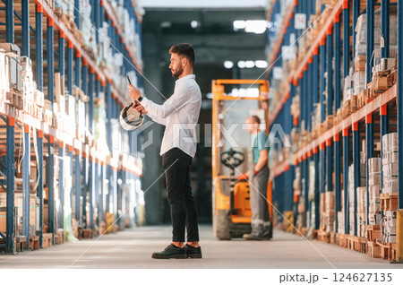 With tablet in hands. Storage worker is in the warehouse with bunch of products 124627135