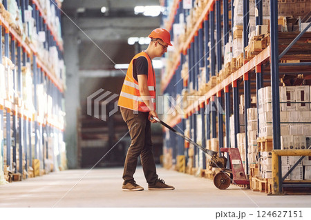 Side view of warehouse worker that is in uniform and hard hat working with cargo 124627151