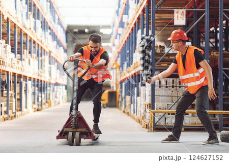 Man riding trolley platform. Having fun. Two storage workers is in the warehouse 124627152