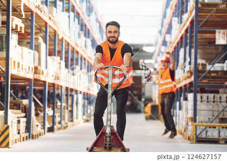 Having fun by using trolley platform. Two storage workers is in the warehouse Having fun by using trolley platform. Two storage workers is in the warehouse 124627157