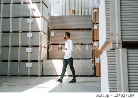 Holding tablet and checking the data. Storage worker is in the warehouse with bunch of products 124627184
