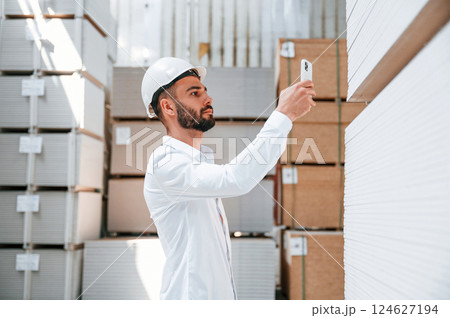 In white hard hat. Storage worker is in the warehouse with bunch of products In white hard hat. Storage worker is in the warehouse with bunch of products 124627194