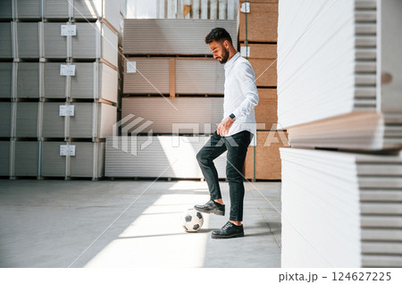 Taking a break, playing with soccer ball. Storage worker is in the warehouse with bunch of products Taking a break, playing with soccer ball. Storage worker is in the warehouse with bunch of products 124627225