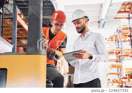 With tablet and cargo moving transport. Two storage workers is in the warehouse With tablet and cargo moving transport. Two storage workers is in the warehouse 124627391