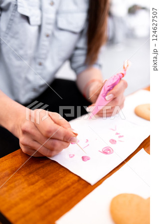 Female decorating cookies with pink icing using toothpick on wooden table Female decorating cookies with pink icing using toothpick on wooden table 124627507