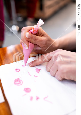 Hand decorating with pink icing on paper using piping bag Hand decorating with pink icing on paper using piping bag 124627510