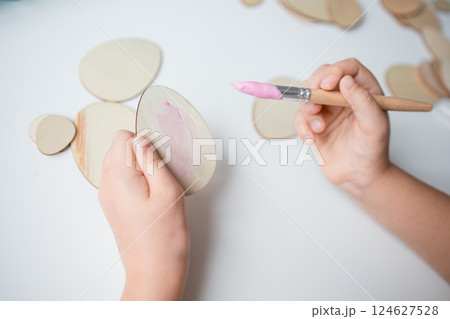 Child painting Easter wooden egg shapes with pink paintbrush on white surface Child painting Easter wooden egg shapes with pink paintbrush on white surface 124627528