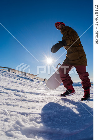 Snowboarder walking against blue sky 124628122