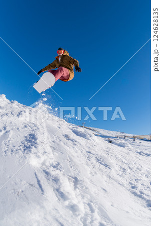 Snowboarder jumping against blue sky 124628135