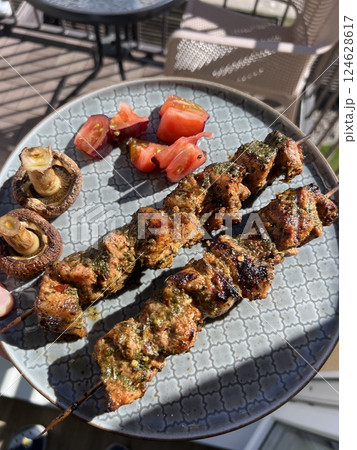 Photo of souvlaki on the chargrill. Meat strung on skewers is fried in the camp at sunset. Smoke rises from the grill. 124628617