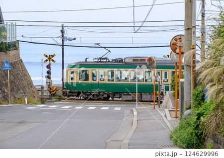 海沿いの踏切を通過する江ノ電、鎌倉、鎌倉高校前駅、坂の上からの風景、聖地巡礼 124629996