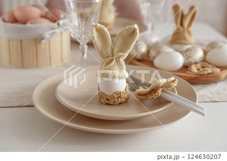 Festive Easter table setting with Easter bunny made from egg and knitted ears. Easter celebration concept Festive Easter table setting with Easter bunny made from egg and knitted ears. Easter celebration concept 124630207