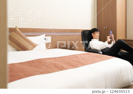 出張先ホテルでスマホ操作するビジネスマン 出張先ホテルでスマホ操作するビジネスマン 124630523