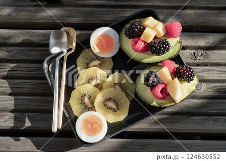 Top view of vibrant healthy food with blackberry, redberry and mango on avocado with golden kiwi and boiled egg is eating colorful on ceramic dish. 124630552