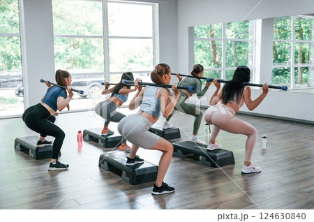 With stick behind the back in hands. Group of women practicing fitness in the gym 124630840