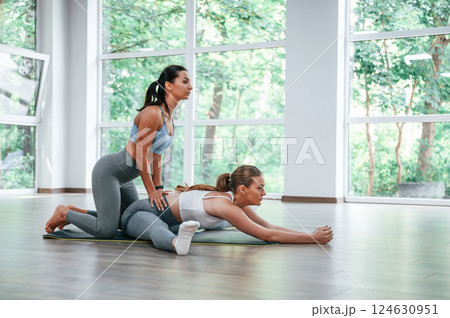 Stretching the legs. Female trainer helping woman with exercises in the gym Stretching the legs. Female trainer helping woman with exercises in the gym 124630951