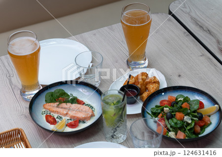 Delicious Gourmet Meal with Fresh Salmon, Crispy Appetizers, Green Salad and Refreshing Beverages Served on a Wooden Table Delicious Gourmet Meal with Fresh Salmon, Crispy Appetizers, Green Salad and Refreshing Beverages Served on a Wooden Table 124631416