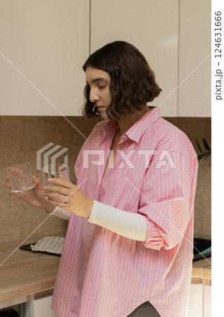 A young woman in a pink shirt is stacking clean glasses in the kitchen A young woman in a pink shirt is stacking clean glasses in the kitchen 124631666
