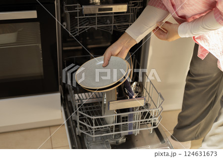 female hands in the frame are putting plates into the dishwasher 124631673