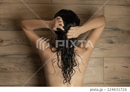 young woman in bathroom massaging long dark curly hair in shower, spa and beauty concept 124631728