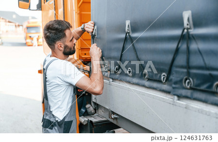 Checking the ropes. Man in unifrom doing service for big truck vehicle Checking the ropes. Man in unifrom doing service for big truck vehicle 124631763