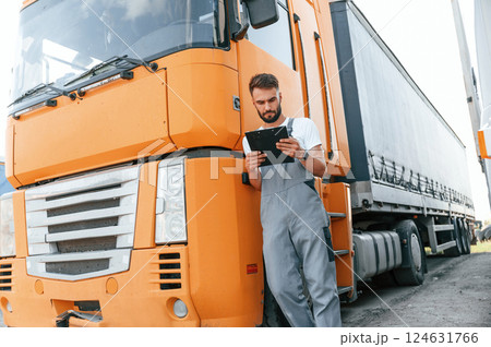Holding notepad. Man in unifrom doing service for big truck vehicle Holding notepad. Man in unifrom doing service for big truck vehicle 124631766