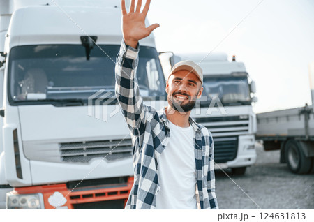 Showing hello gesture by hands and smiling. Young truck driver is with his vehicle at daytime Showing hello gesture by hands and smiling. Young truck driver is with his vehicle at daytime 124631813