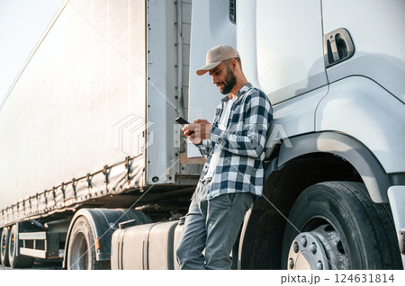 Leaning by the vehicle and using phone. Young truck driver is at daytime 124631814