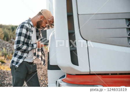 Feeeling tired. Using smartphone. Young truck driver is with his vehicle at daytime Feeeling tired. Using smartphone. Young truck driver is with his vehicle at daytime 124631819