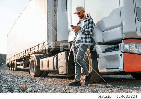 Leaning by the vehicle and using phone. Young truck driver is at daytime 124631821