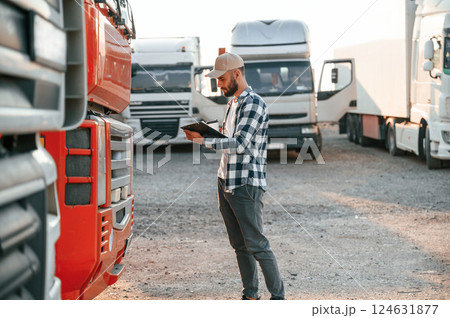 With cup of drink and notepad. Young truck driver is with his vehicle at daytime 124631877