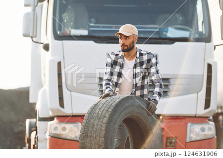 Working with damaged tire. Young truck driver is with his vehicle at daytime Working with damaged tire. Young truck driver is with his vehicle at daytime 124631906