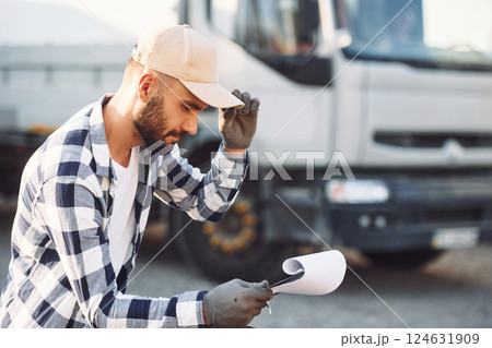 Sitting and reading the document. Young truck driver is with his vehicle at daytime Sitting and reading the document. Young truck driver is with his vehicle at daytime 124631909
