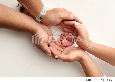A father and mother hold the feet of a newborn child in a white blanket on a white background.. The feet of a newborn in the hands of parents. Photo of foot, heels and toes.The palms of the parents. A father and mother hold the feet of a newborn child in a white blanket on a white background.. The feet of a newborn in the hands of parents. Photo of foot, heels and toes.The palms of the parents. 124632355