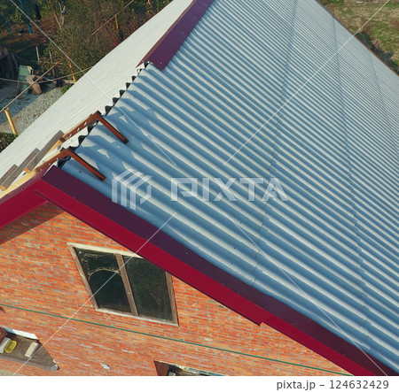Construction of roof of the house, a wooden staircase to the roof with a hook, the corners of the skates of the red metal profile. Construction of roof of the house, a wooden staircase to the roof with a hook, the corners of the skates of the red metal profile. 124632429