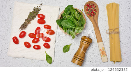 Wooden bowl with spinach, cherry tomatoes on a wooden plate, spoon with spices, uncooked spaghetti tied with twine Wooden bowl with spinach, cherry tomatoes on a wooden plate, spoon with spices, uncooked spaghetti tied with twine 124632585